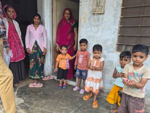 Local women and young children gather outside a rural home in colorful clothing