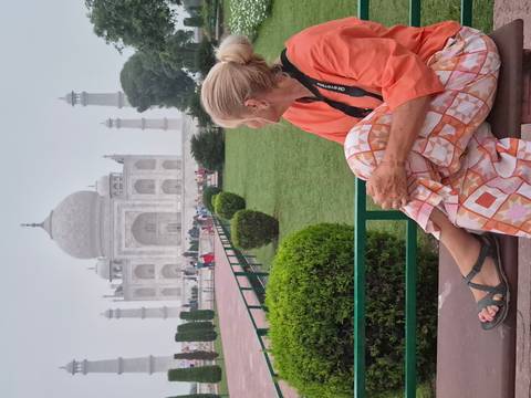Traveler sits on bench admiring the misty Taj Mahal across manicured gardens