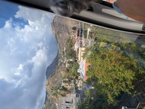 View from a cable-car window over a Mediterranean hillside town beneath dramatic clouds.