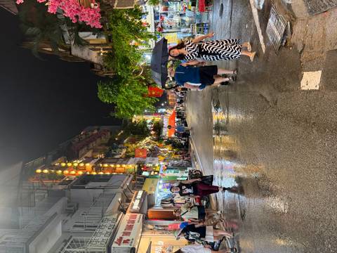 Rain-soaked evening street scene in Hanoi’s Old Quarter with neon lights and pedestrians carrying umbrellas.