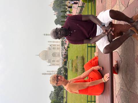 Couple seated on a bench with the Taj Mahal’s white marble domes softly visible in the hazy background.