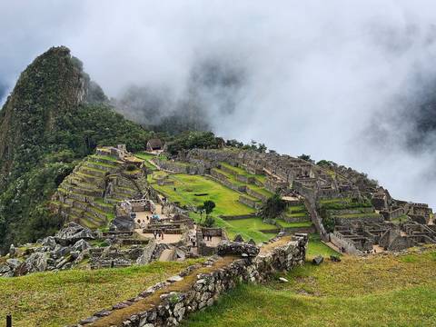 Machu Picchu's terraced ruins emerge from drifting cloud with Huayna Picchu peak looming.