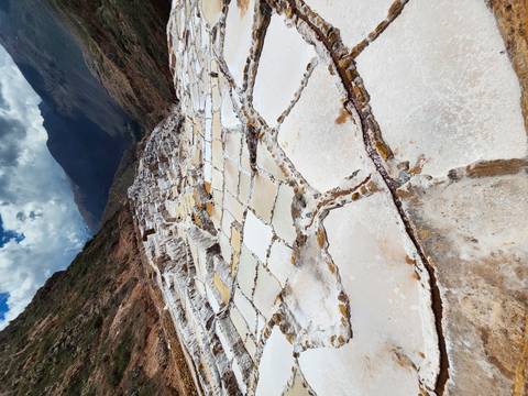 White stepped salt pans of Maras glisten along a dramatic Andean valley slope.