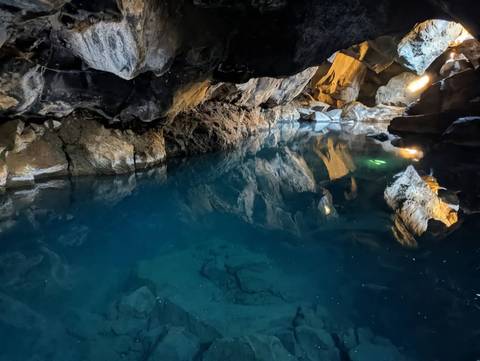 Crystal-clear geothermal pool inside a volcanic lava cave with rock walls lit by lamps