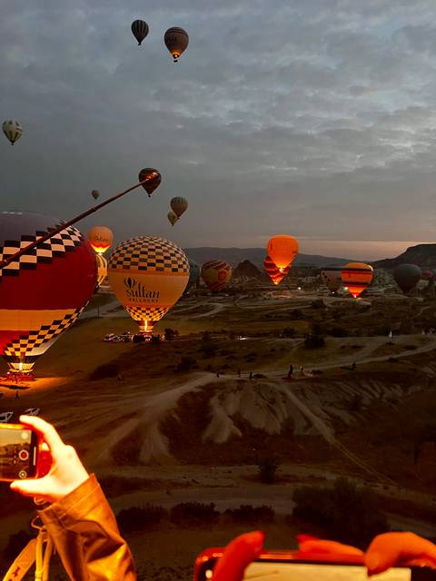 Dozens of illuminated hot-air balloons prepare for dawn ascent over Cappadocia in the predawn darkness.