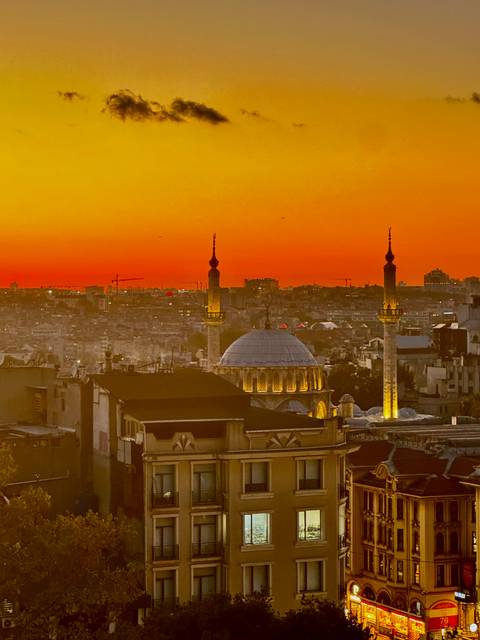 Fiery orange sunset silhouettes domes and minarets over a sprawling city skyline.