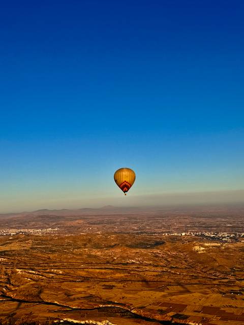 Yellow balloon floats solo high above Cappadocian plateau under a clear blue sky.