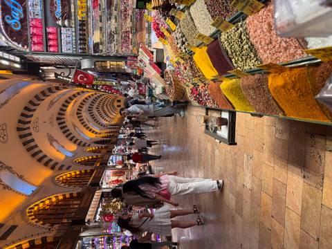 Busy indoor spice bazaar lined with colorful mounds of herbs and sweets under ornate arched ceiling.