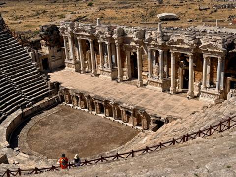 Panoramic view of well-preserved stone Roman theatre with tiered seating and stage columns.