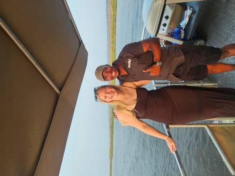 Smiling tourist and guide pose on the deck of a river boat with wilderness backdrop.