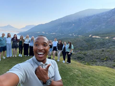 Selfie of enthusiastic guide with group against dramatic mountain landscape and blue sky.
