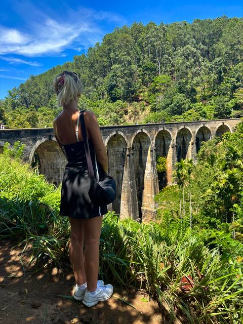 A traveler looks out over the famous Nine Arches Bridge amid lush jungle greenery in Ella, Sri Lanka.