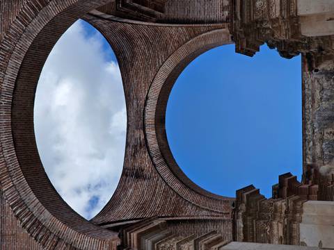 Looking up through a massive brick archway of an Antigua ruin to a patch of blue sky and clouds.