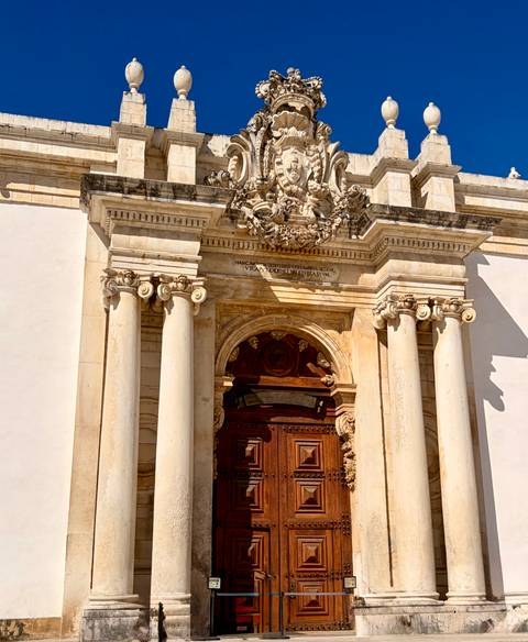 Classical stone doorway with ornate columns and sculpted crest in bright sunlight.