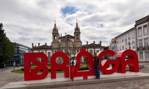 Two travelers stand by bold red BRAGA letters with historic church behind.