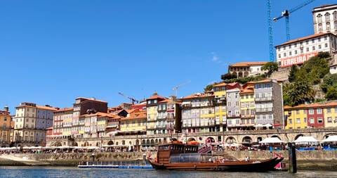Colorful riverside houses and a traditional wooden boat on the Douro River under blue sky.