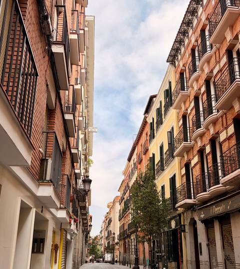 Narrow Madrid street framed by tall brick and pastel buildings with balconies.