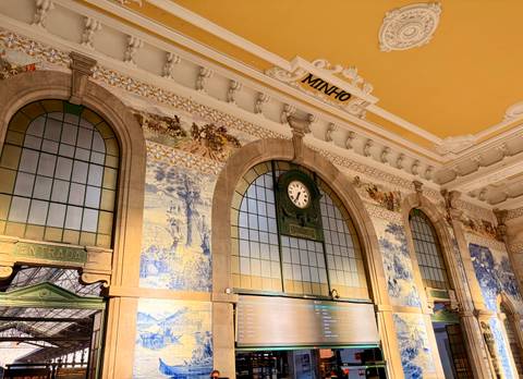 Interior hall with ornate azulejo tile murals, high arched windows and classic station clock.