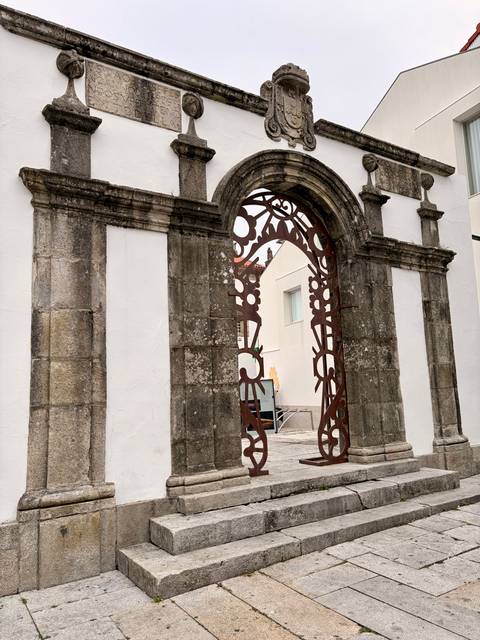 Stone archway with decorative rusty iron gate set against white walls.