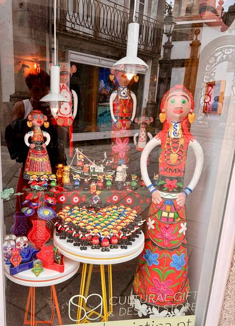Shop window filled with colorful folk art dolls, ceramics and reflections of the street.