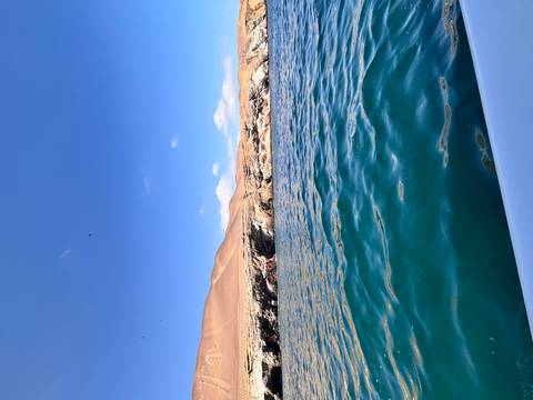 Deep blue Pacific waters with arid coastal cliffs and desert hills in the background under clear skies.