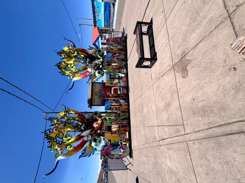 Colorful Candelaria festival sign decorated with large artistic masks on a plaza under bright blue sky.