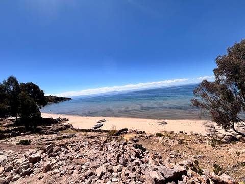 Quiet sandy beach on Lake Titicaca with small boats and clear blue water stretching to the horizon.