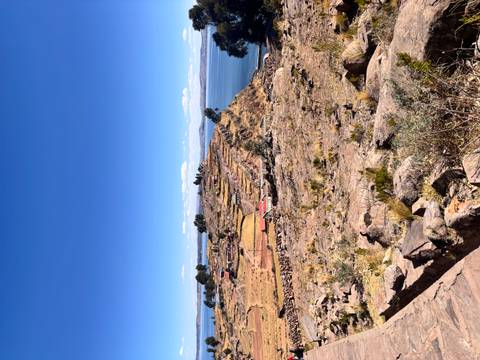 Dry terraced ridge stretching into sparkling blue water of a high-altitude lake under clear sky.
