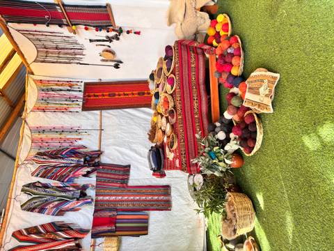 Indoor display of vibrant woven textiles and baskets of dyed wool balls on artificial grass.