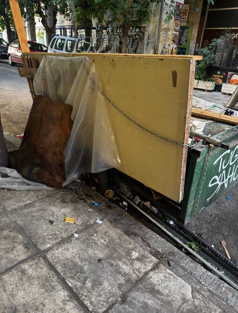 Urban alley corner cluttered with discarded scrap and rubbish beside a graffitied cart.
