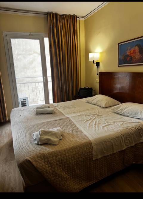 Modest hotel room featuring a made double bed, balcony door and striped curtains.