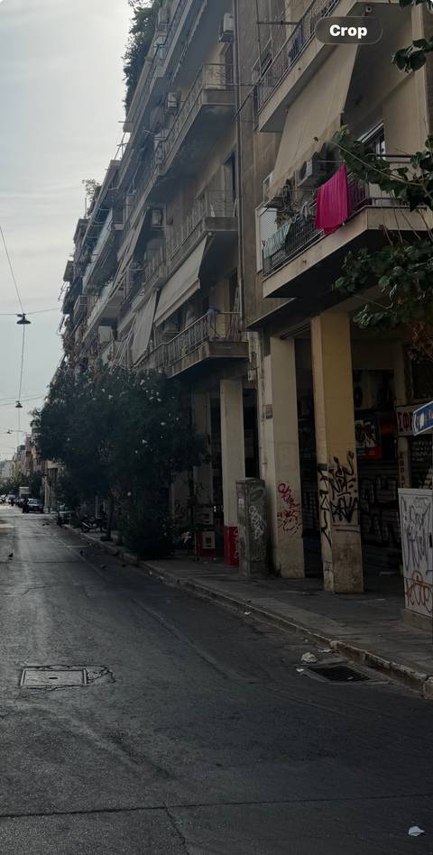 Graffitied urban street lined with drab, ageing apartment blocks and overgrown trees.