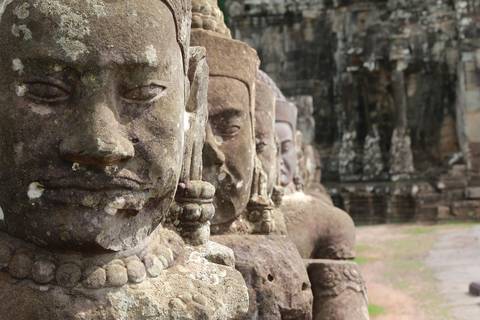 Row of ancient sandstone guardian statues with serene faces at Angkor temple complex.