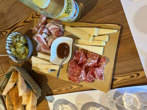 Wooden board loaded with regional cold cuts, cheeses and jam set on a rustic dining table.