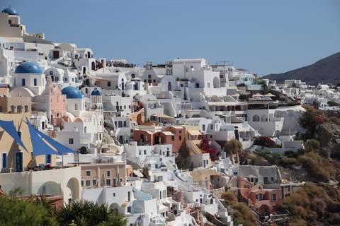 Iconic white-washed houses and blue-domed churches clustered on the cliffs of Oia, Santorini under clear sky.