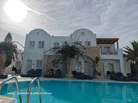 Boutique Cycladic hotel with pool and loungers, guests relaxing beneath light overcast sky.