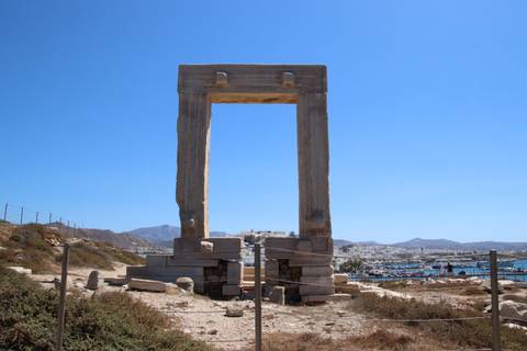 Ancient marble Portara gate of Naxos standing alone on a hilltop with harbor and town in background.