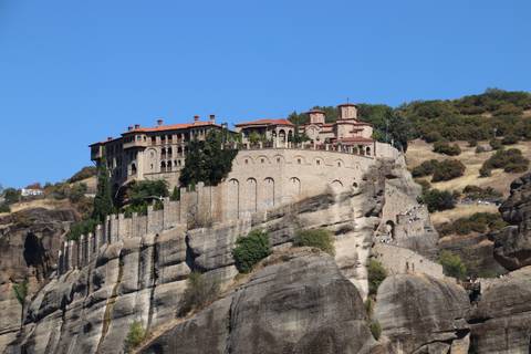 Monastery perched atop towering sandstone cliffs at Meteora under clear blue sky.