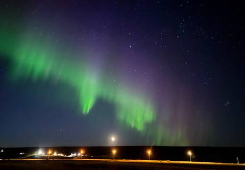 Northern Lights dancing in green and purple hues over a dark horizon and star-filled sky.