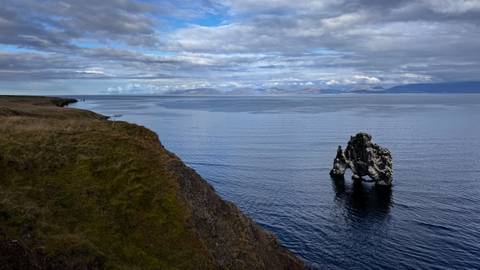Solitary basalt sea stack, Hvitserkur, rising from calm blue waters beside grassy cliff edge.