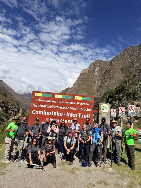 Hiking group posing at the Camino Inka – Inka Trail welcome sign beside rugged valley walls.
