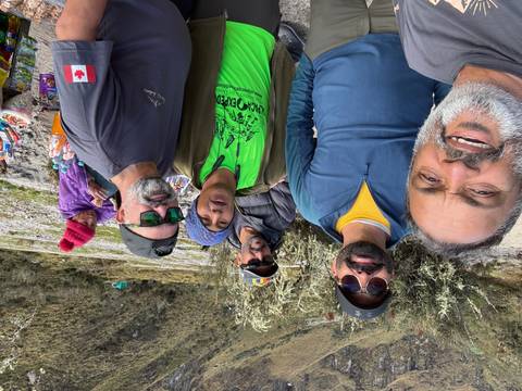 Casual selfie of trekkers at a rest stop with snacks table and mountain vegetation around.