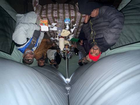 Campers sitting along a long table inside a canvas tent during evening meal, lit by flash.