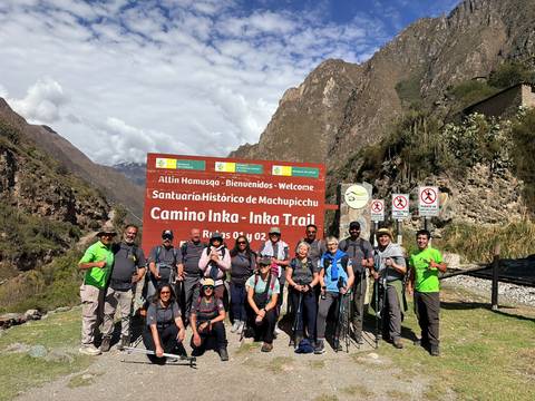 Large group of hikers smiling at Inca Trail signage before starting their trek.