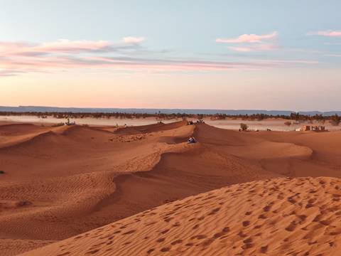 Sunrise glow over sand dunes of the Sahara near Merzouga with low mist hovering and distant riders.
