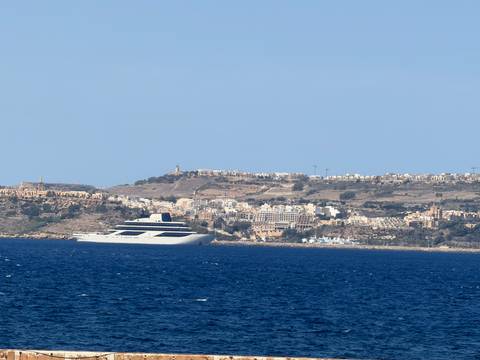 Distant coastal Maltese town with large luxury yacht on deep blue Mediterranean Sea