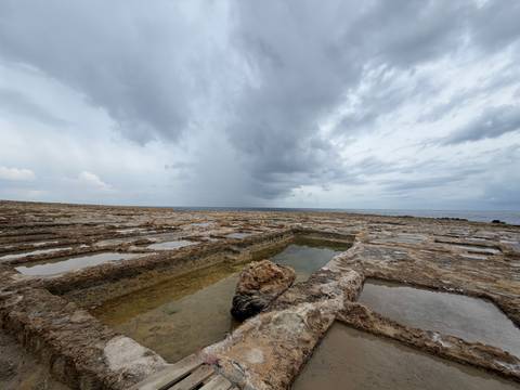 Rocky salt pans on a Maltese shoreline with dramatic overcast sky and distant sea