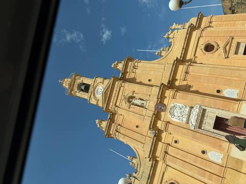 Yellow limestone church facade with clock tower photographed from a low angle against blue sky