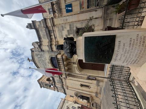 Bust of Saverio Cassar with Maltese flag in front of stone church building