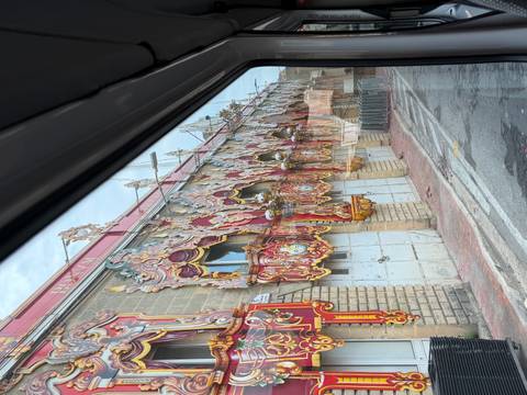 Colorful ornate festival facade panels stored along a street, photographed through a bus window